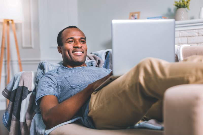 Man relaxing on the couch with laptop, feeling stress-free while preparing taxes for easy filing this tax season.