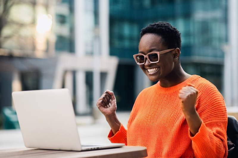 A happy woman working on her laptop, smiling as she explores tips to boost her tax refund for next year.