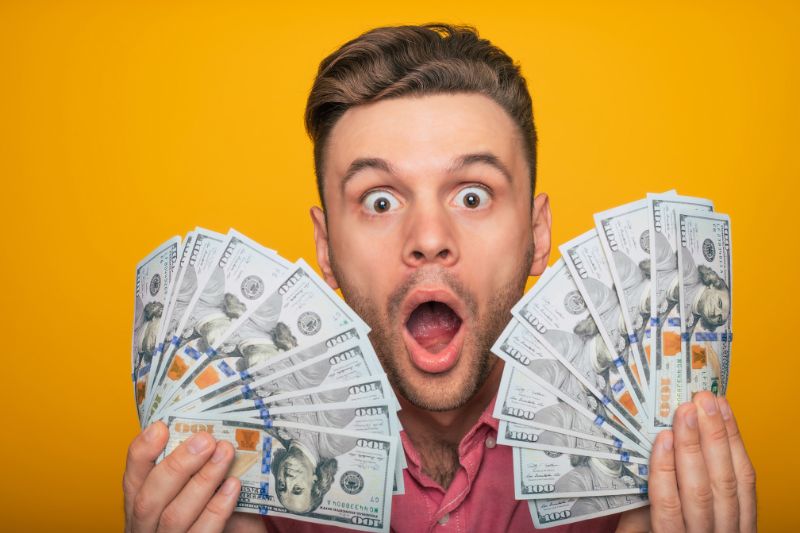 Man holding a fan of money in each hand, looking surprised, representing the excitement of estimating your tax refund with a step-by-step guide.