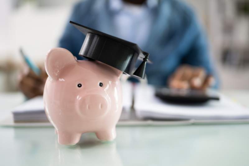 Piggy bank with a graduation cap, symbolizing the student loan interest deduction, with a blurred background of a man working on his budget.