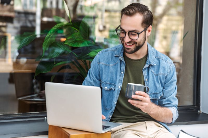 Man sitting outside with coffee, using his laptop to learn about the Premium Tax Credit and how it can help lower health insurance costs.