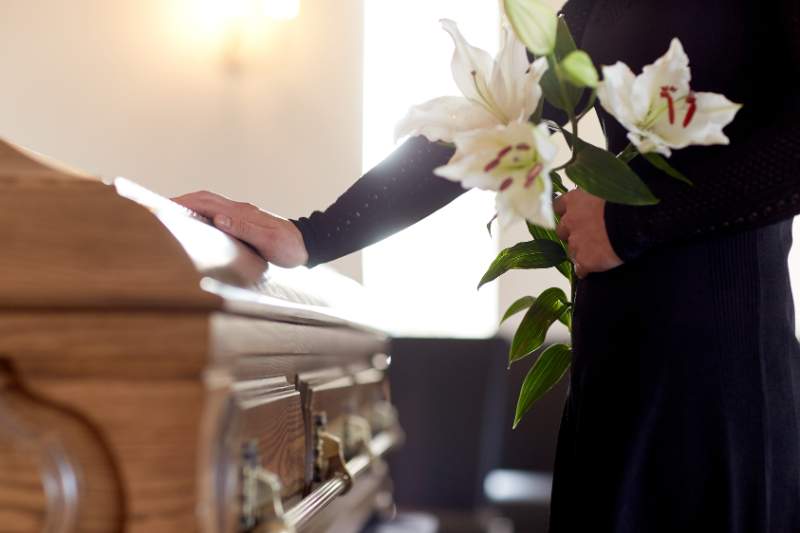 Man with flowers touching a casket, reflecting funeral expenses and tax deductions for a deceased loved one.