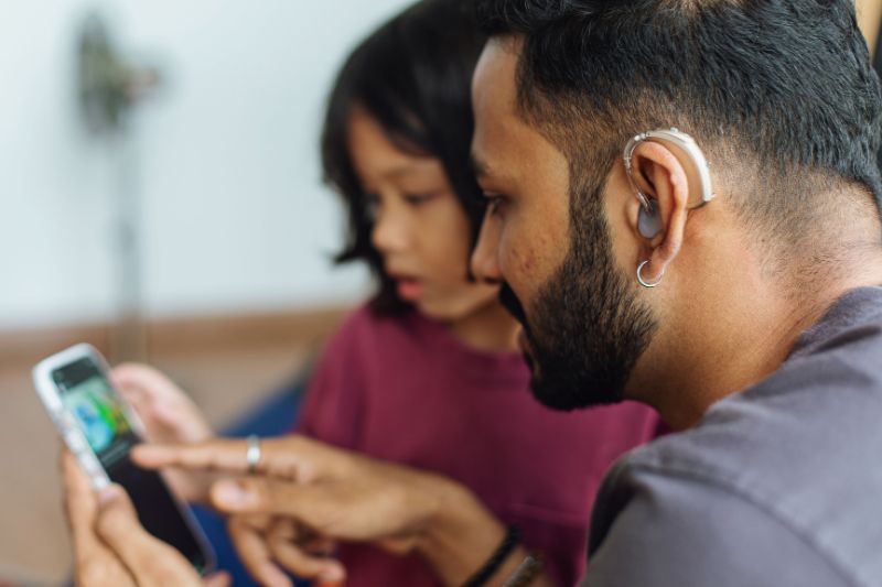 A man with hearing aids and a child looking at a phone, highlighting the role of hearing aids in daily life and their potential tax deductibility.