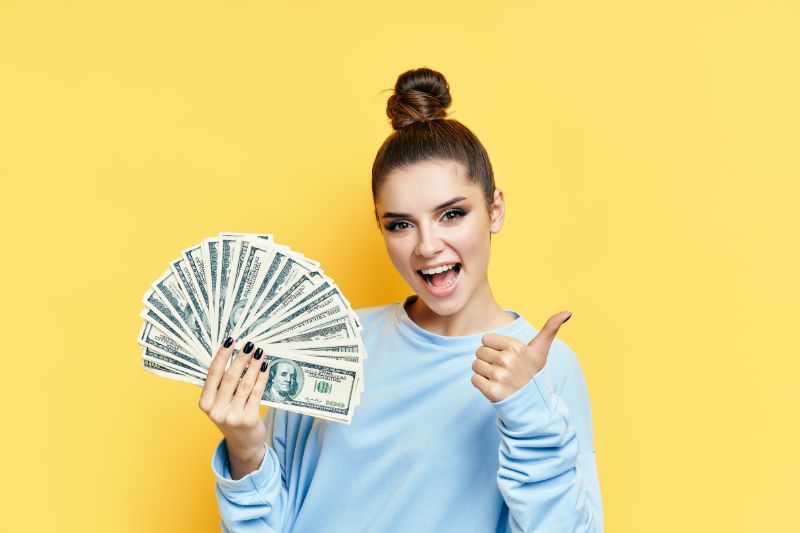 Smiling woman holding a fan of money, symbolizing tax-saving tips and strategies to reduce your tax bill and maximize savings.