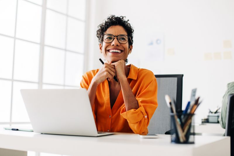 Happy woman sitting at her desk with a laptop, exploring whether she needs to file a tax return.