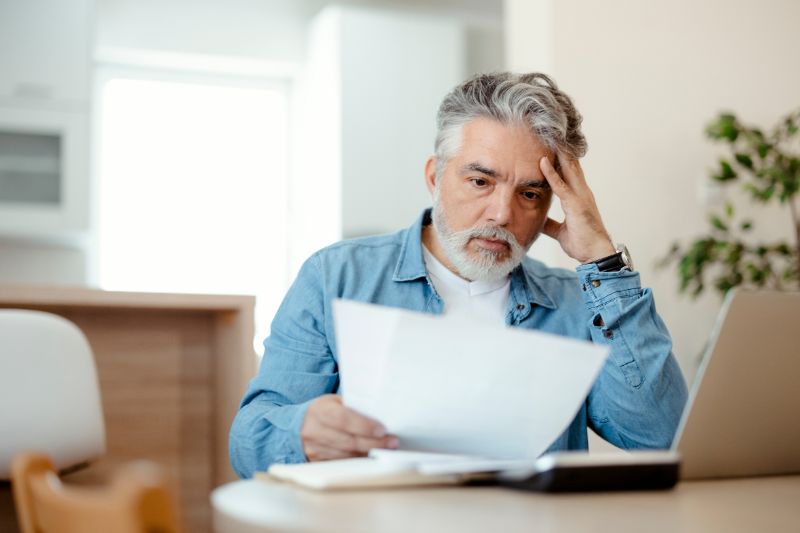 Middle-aged man looking confused while reviewing papers, symbolizing the complexities of filing taxes for a deceased person.