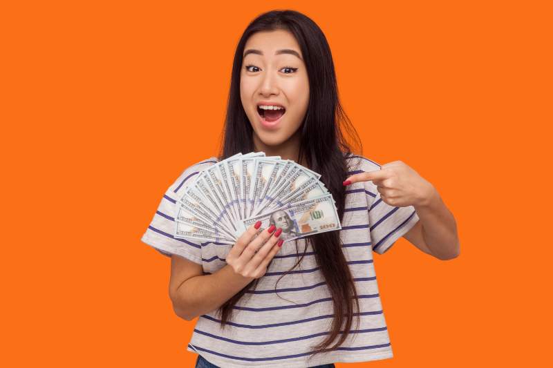 Woman holding a fan of money and pointing at it, representing how to get a bigger tax refund with no dependents by using smart tax strategies.