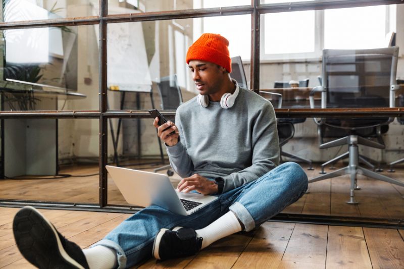 A person sitting on the floor, looking at his phone and laptop, learning what non-taxable income is for better financial understanding.