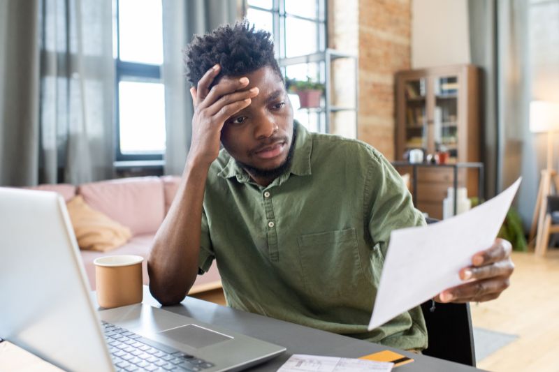 Stressed man sitting at desk, looking at tax paper, illustrating the challenges of filing taxes late and the importance of timely action.