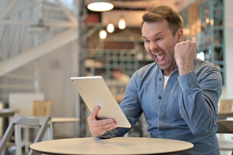 Excited man celebrating with a fist pump while holding a tablet, symbolizing success in reducing taxable income through effective strategies.