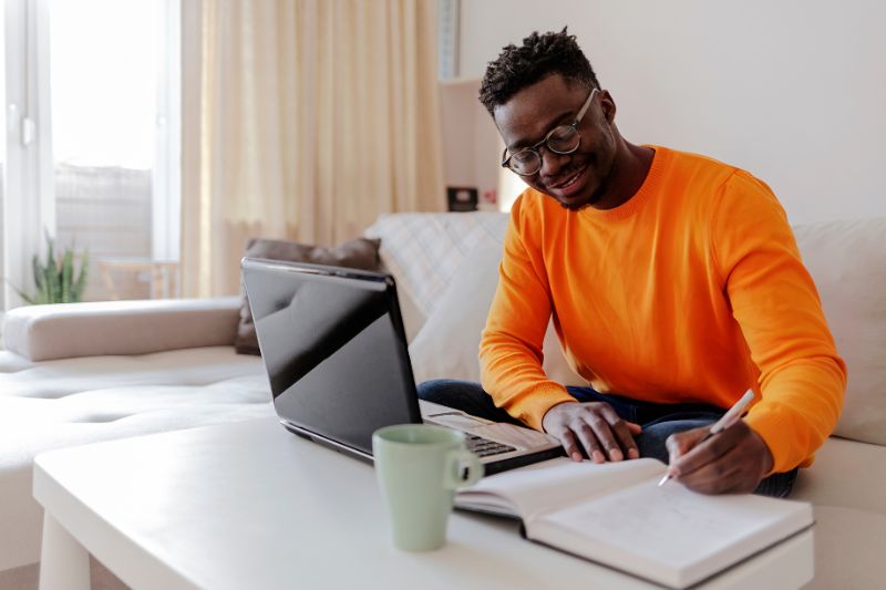 A man working at his desk, taking notes in a book while researching the Qualified Business Income (QBI) deduction on his laptop.